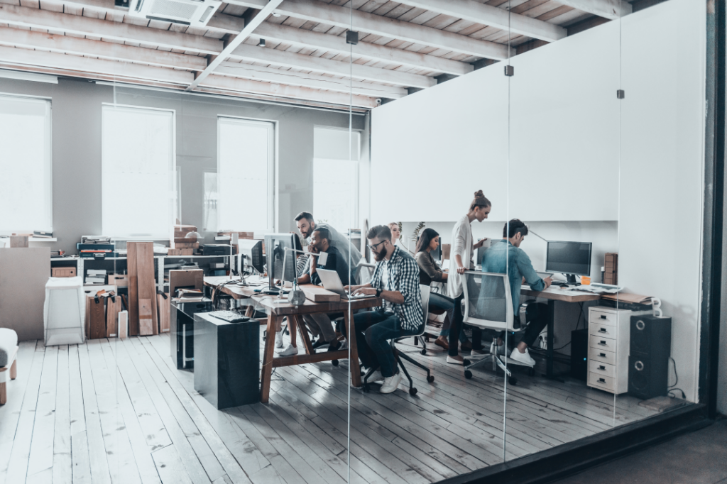 Group of professionals working together at desks in a modern office with wooden floors and large windows.